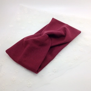 Detail view of burgundy ribbed knit headband with cross-knot design on lace background