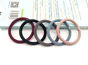 Detail of five high-elasticity braided hair ties in assorted muted colors with matte buckles