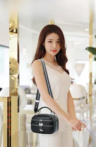 Detail of black leather crossbody bag with silver zipper charms and woven shoulder strap