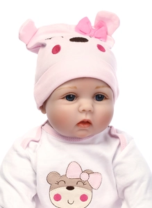 Close-up of lifelike newborn doll with blue eyes wearing a pink bear hat and white outfit