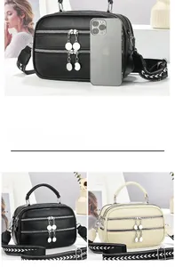 Detail of multi-zipper leather handbag with wide arrow strap and metal pendant