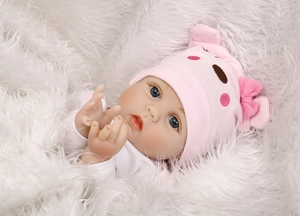 Close-up of lifelike reborn baby doll in pink pig hat lying on soft white plush blanket