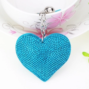 Close-up of sparkling blue rhinestone heart charm with silver chain on a porcelain cup