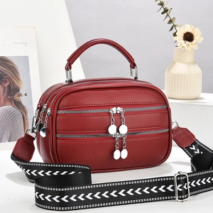 Fashionable burgundy leather handbag with woven wide shoulder strap and silver zippers