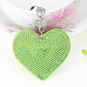 Macro detail of a green heart keychain with sparkling crystals and a silver bell