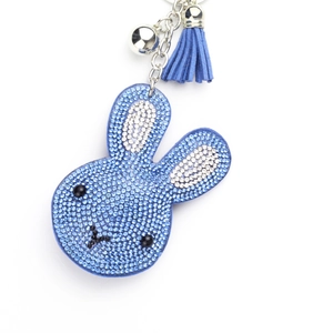 Macro detail of a blue rhinestone bunny keychain with fabric tassel and silver bell