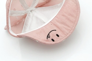 Detail of pink baby baseball hat showing breathable mesh, soft lining and smiley embroidery