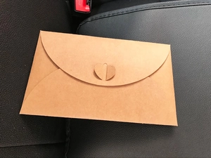 Close-up of brown kraft paper envelope with heart-shaped clasp on a leather surface
