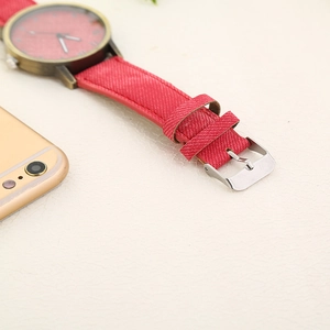 Detail view of red denim fabric watch strap with silver buckle and bronze watch case