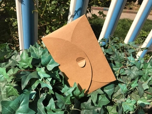 Close-up of brown kraft paper envelope with heart-shaped closure on green ivy leaves