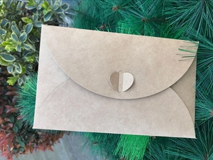 Detail of vintage kraft paper envelope with heart-shaped clasp set against pine needles