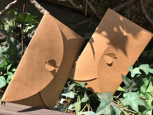 Detail of brown kraft paper envelopes with heart-shaped clasps on a natural leaf background