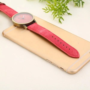 Close-up of a red denim strap watch with bronze case resting on a smartphone surface