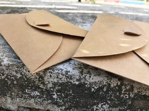 Detail view of 300g kraft paper envelopes with round flaps on a rustic concrete surface