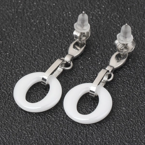 Macro detail of silver stainless steel earrings with white ceramic hollow round drops
