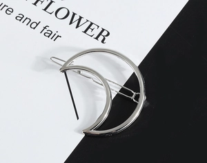 Macro detail of a silver moon-shaped metal hair clip with a smooth polished mirror finish
