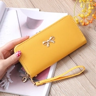 Yellow long zip clutch bag with gold bow clasp and hand strap on aesthetic background