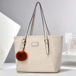 Detail der beigen Handtasche aus Leder mit goldener Schnalle und braunem Plüschanhänger