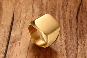 Close-up of a masculine gold stainless steel square signet ring on a wood background