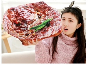 Detail showing the large 3D realistic steak plush pillow held by a person for size display