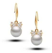 Detail of elegant gold earrings with crystal bow and white pearls on white background