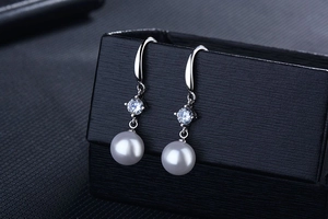 Close-up of elegant pearl drop earrings with round zircon stones on black jewelry box