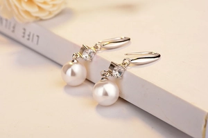 Close-up of elegant white pearl drop earrings with sparkling zircon on silver metal hooks