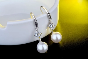 Macro shot of high-quality pearl earrings with sparkling crystal and silver hooks