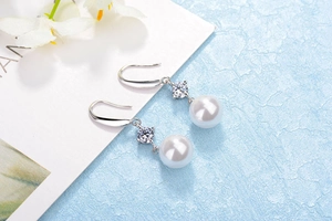 Detailed macro view of white round pearl earrings with zircon inlay on silver hooks