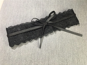 Detail eines schwarzen Spitzen-Taillengürtels mit Kunstlederschleife auf grauem Stoff