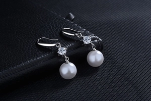 Macro shot of high-quality round white pearl earrings with zircon stones on black leather