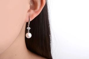 Close-up of white round pearl earring with gemstone inlay on model's ear