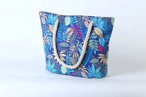Detail of blue canvas tote bag featuring multicolored leaf patterns and rope handles
