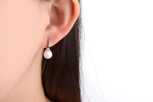 Close-up of a white pearl drop earring with a polished silver hook on a model