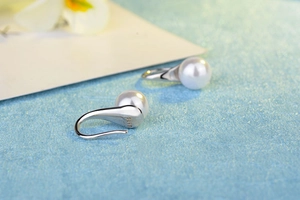 Close-up of S925 sterling silver pearl earring hooks with detailed hallmark on blue surface