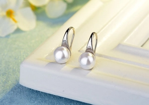 Detailed close-up of white round pearl drop earrings on a minimalist display stand