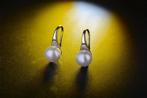 Detailed view of elegant white pearls on silver metal hooks over a dark textured surface