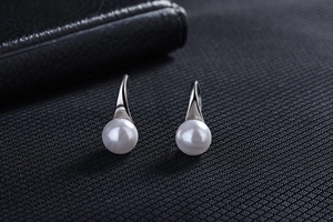 Detail of elegant silver pearl drop earrings featuring round white pearls on dark background