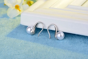 Detailed view of S925 sterling silver pearl earrings with hallmarked hooks on blue background