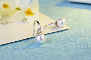 Detailed view of elegant white pearl earrings with silver metal hooks on a soft background
