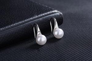 Macro detail of elegant white round pearls with silver hooks on dark leather background