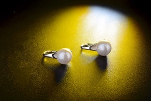 Artistic close-up of pearl earrings with silver base on matte black spotlight background