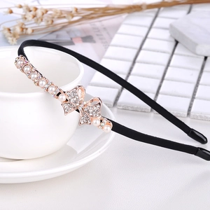 Detail of a black headband with rhinestone bow placed on a white porcelain teacup