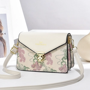 Chic cream crossbody bag with floral embroidery and gold hardware on white stand