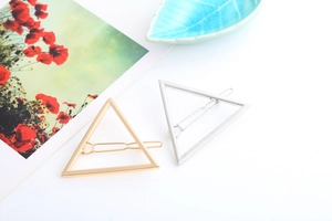 Detailed view of geometric triangle hair clips in polished gold and silver metal finishes