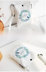 Detail of white canvas crossbody bag featuring teal floral wreath and bird illustration