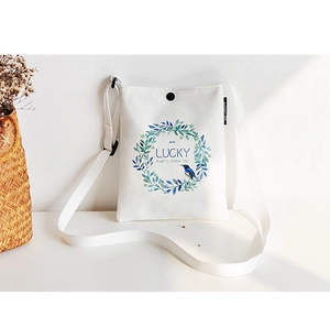 Detail of white canvas crossbody bag featuring a green floral wreath and Lucky print