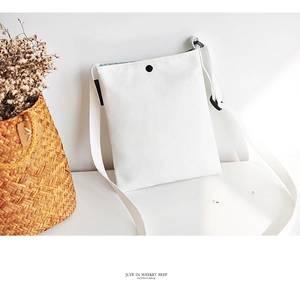 Detail of white canvas crossbody bag featuring a black snap button and adjustable strap
