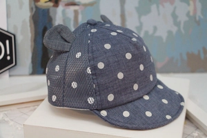 Blue baby baseball cap with white polka dots and cute ears on a geometric stand