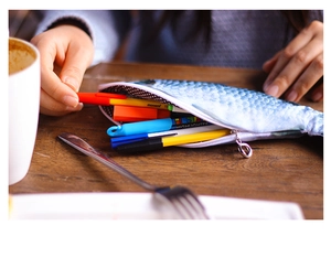 Hands opening a realistic fish-shaped pencil case on a desk to show inner capacity